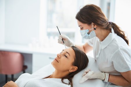 Concentrated skilled female beauty therapist spreading a cosmetic product over a young Caucasian woman forehead